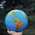 Crop anonymous person reaching out hand and showing Earth globe against green plants in daytime