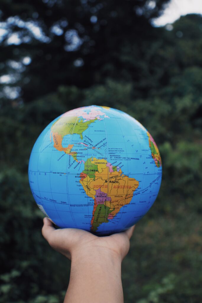 Crop anonymous person reaching out hand and showing Earth globe against green plants in daytime