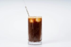 A chilled glass of iced coffee with a straw against a clean white background.