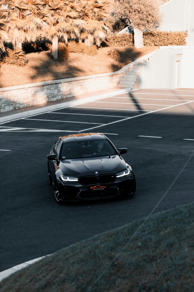 A stylish black car parked in an empty lot under golden sunlight, showcasing modern urban architecture.