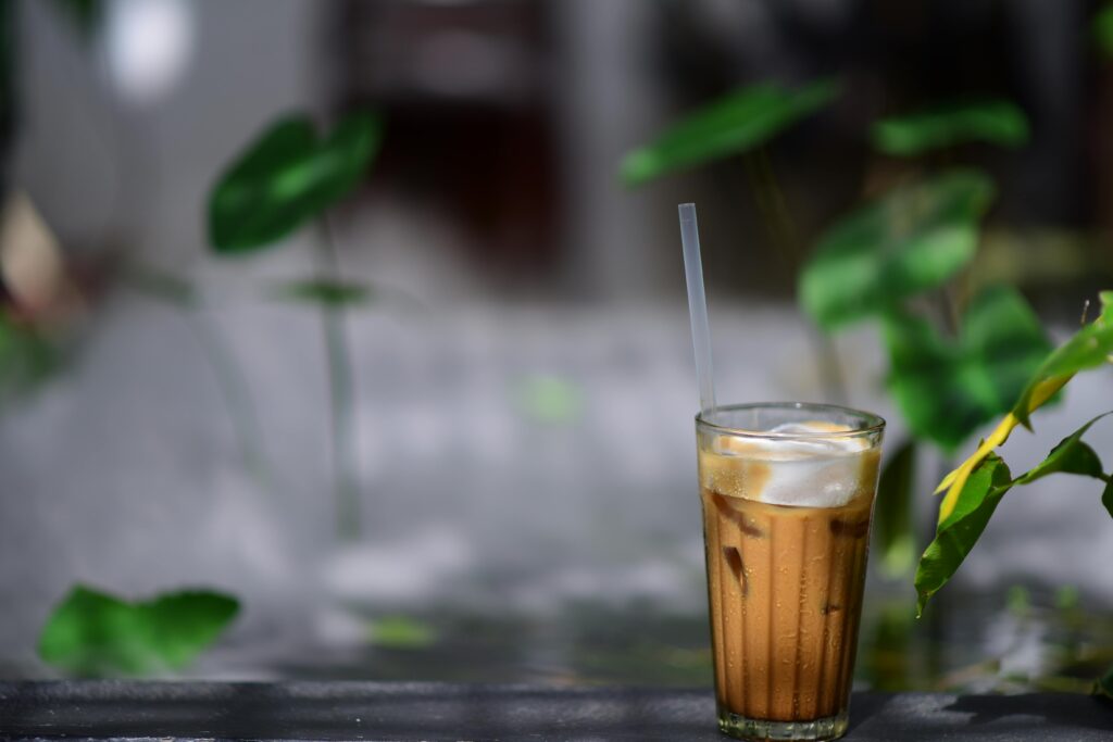 Refreshing iced coffee with straw amidst greenery in outdoor setting.