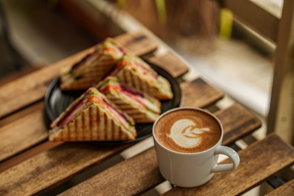 Delicious coffee with latte art and sandwiches on a rustic wooden table setting.