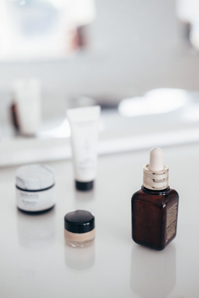 Bottle of aroma oil near jars of creams and tube of lotion against shiny mirror