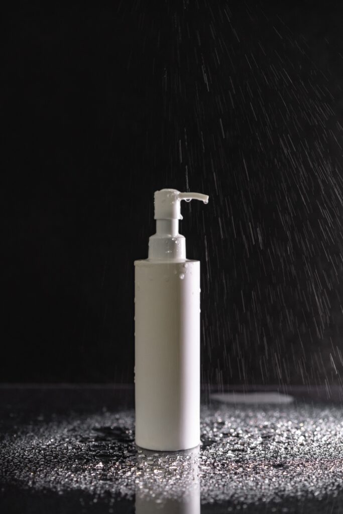 A pump lotion bottle stands amidst water droplets against a black background.