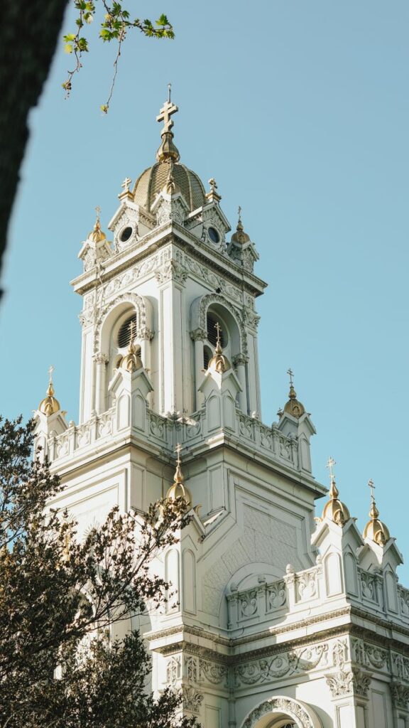 Beautiful white Orthodox church tower with golden details set against a clear blue sky.